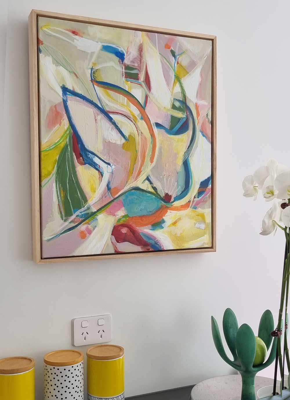 Budgie Bustle abstract painting by Kirsty Black in natural cedar frame hung on white kitchen wall above canisters and orchid