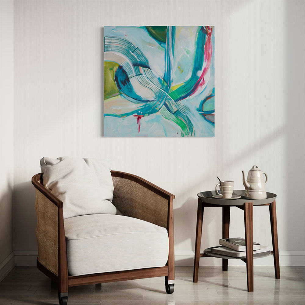 Original abstract painting in aqua, teal and green tones displayed above a rattan armchair with white cushion in a sun-drenched minimalist room
