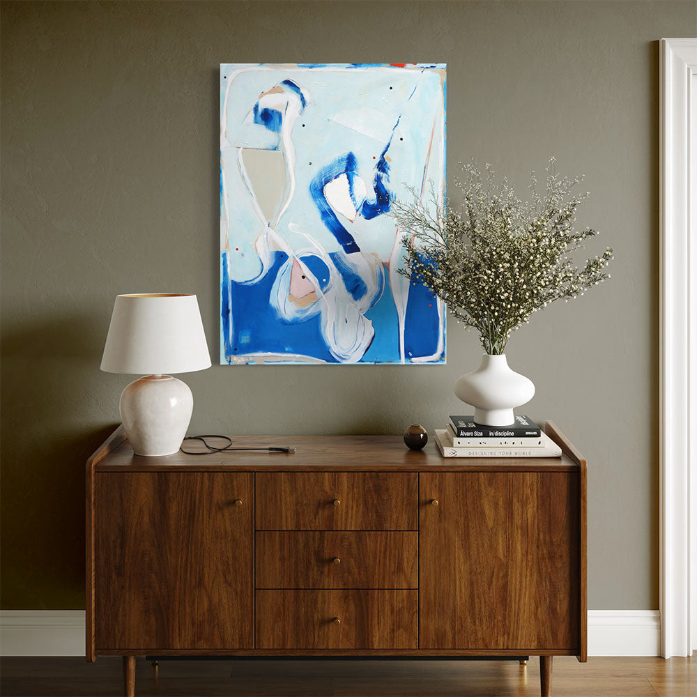 Pang Wangle abstract painting by Kirsty Black hung on olive green wall above mid-century walnut sideboard with white ceramic table lamp, stacked art books and white vase with dried flower stems