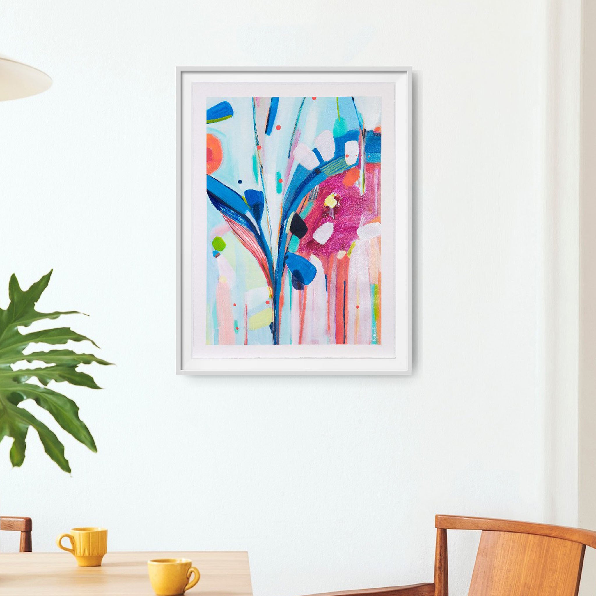 Framed abstract artwork with colorful design on a white wall above a table