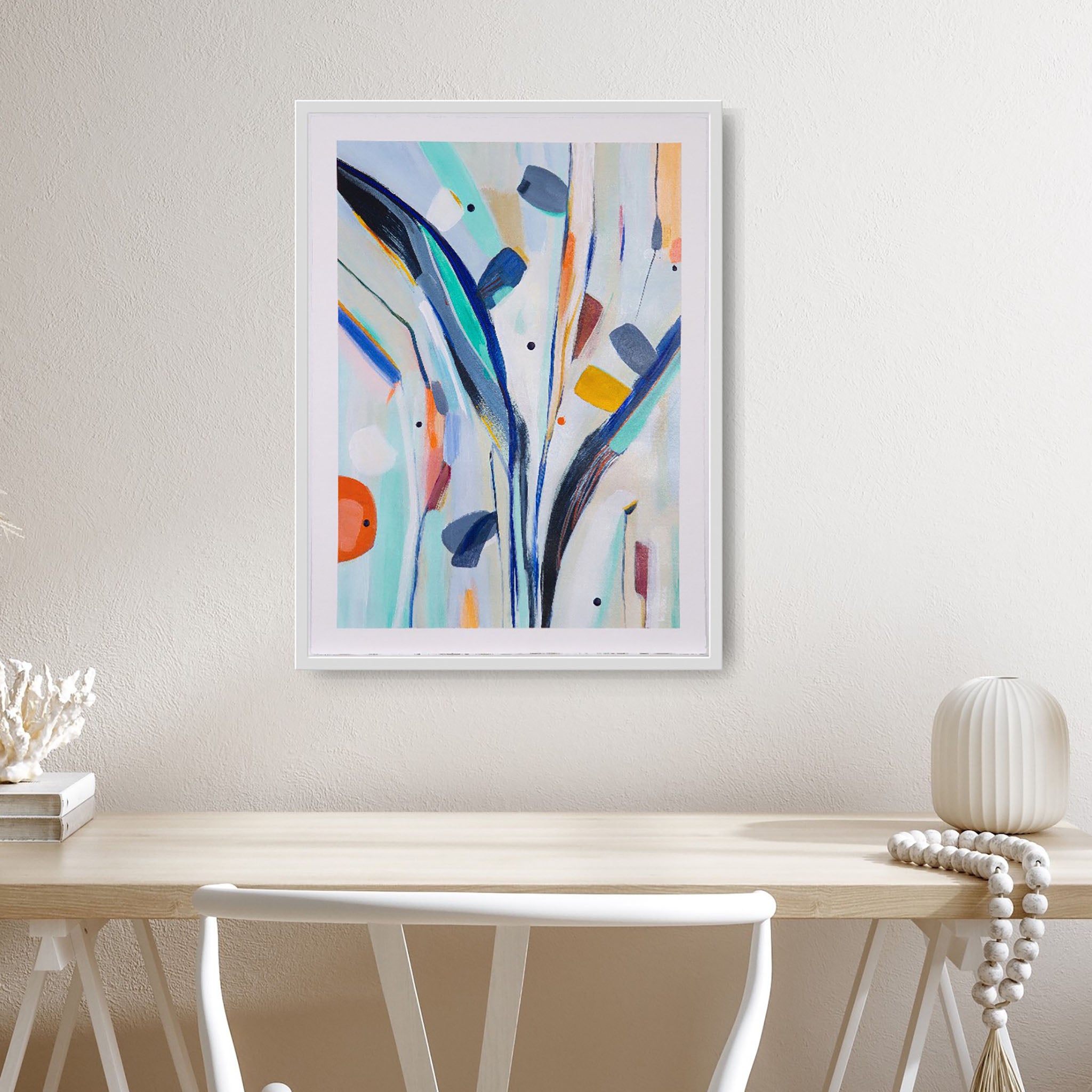 framed abstract painting on paper in blues with a white frame hanging above a desk
