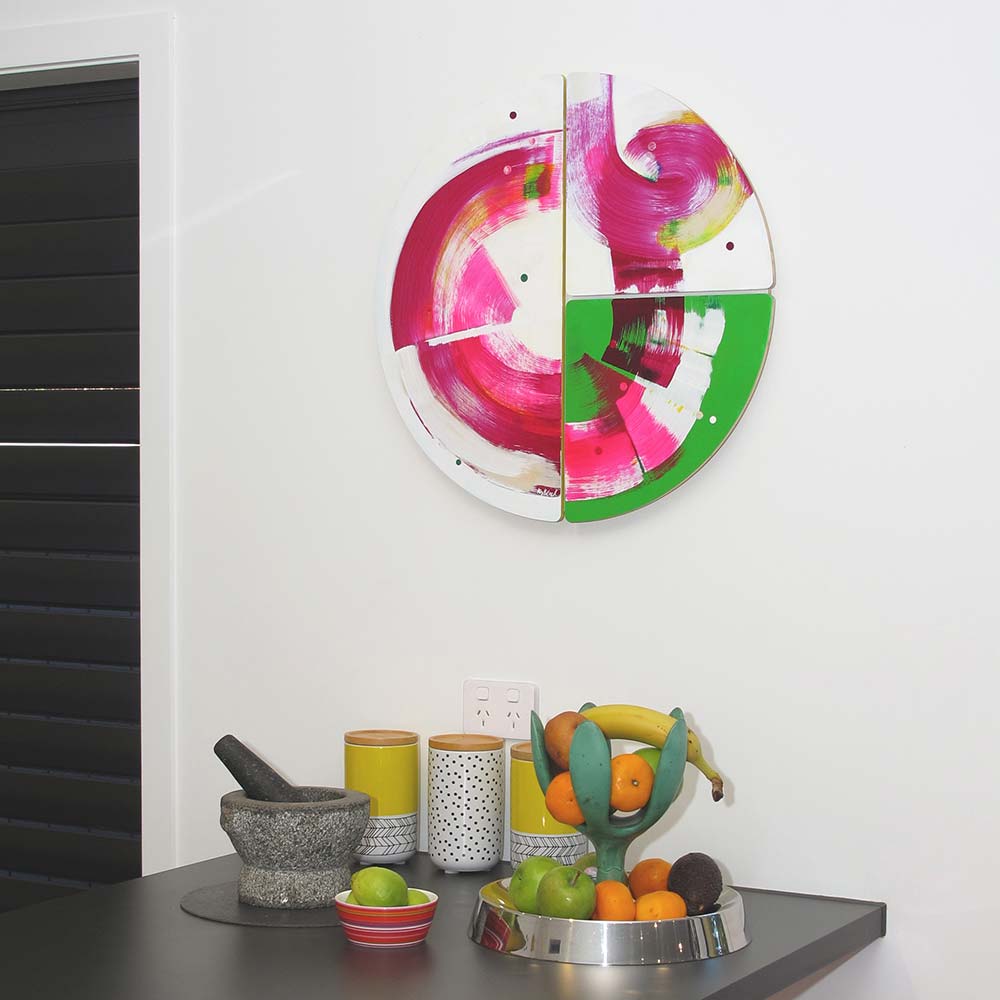 Roller Disco Dames wall sculpture by Kirsty Black installed above a dark kitchen bench with fruit bowl, canisters and mortar and pestle, the vivid magenta and green forms energising the contemporary interior.
