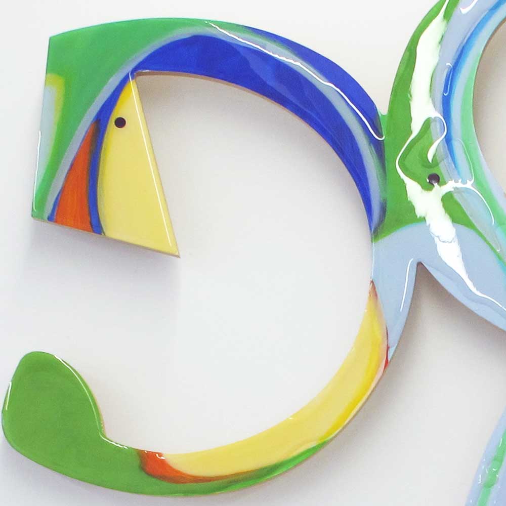 Detail of Cartwheeling Crustacean wall sculpture by Kirsty Black showing the large C-shaped left arm in cobalt blue, green and yellow with orange accent, the open negative space and glossy resin surface clearly visible.