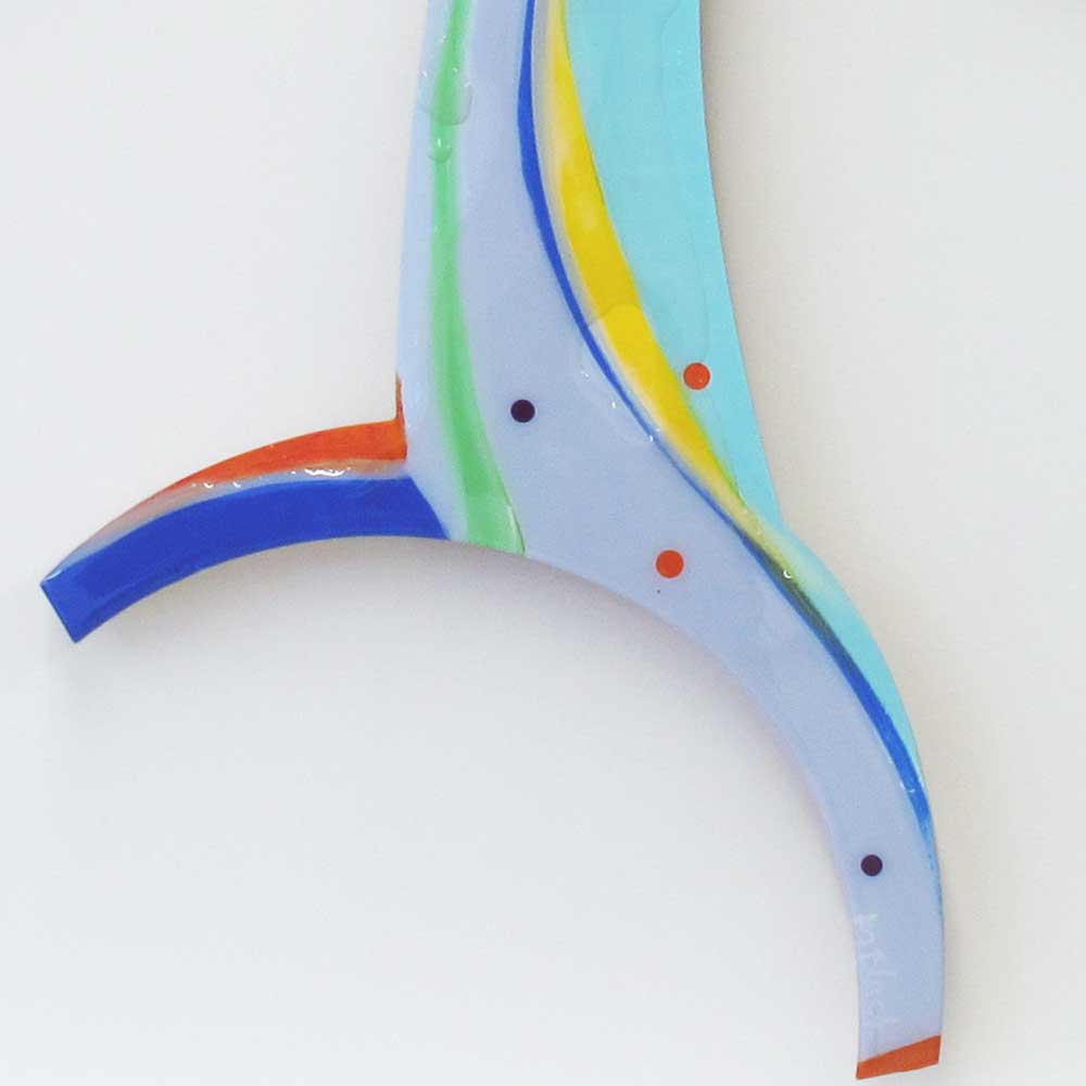 Detail of Cartwheeling Crustacean wall sculpture by Kirsty Black showing flowing lower arms in pale blue with layered green, yellow and orange stripe detailing and scattered navy and orange dot accents.