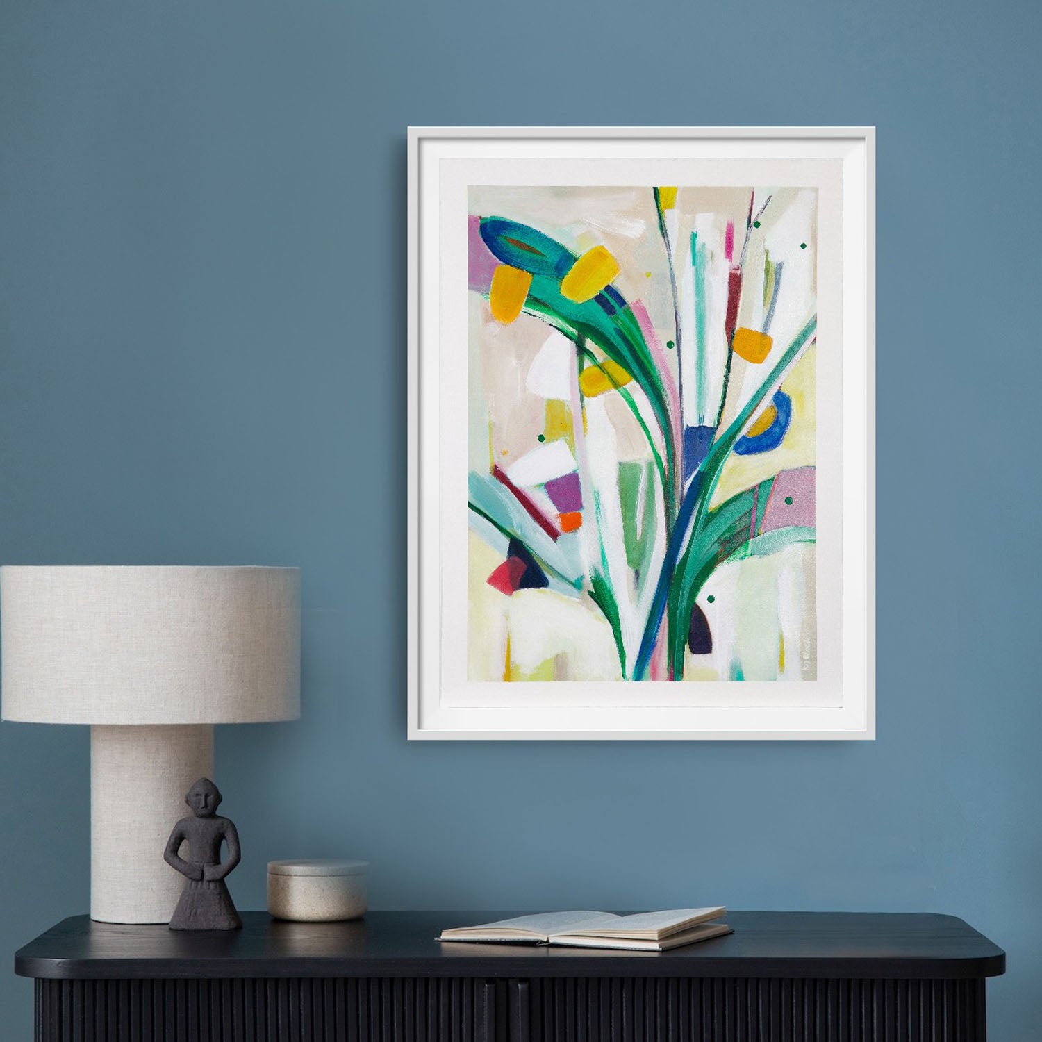 Joyful abstract artwork on paper in a  float mounted with a white frame hanging on a blue wall