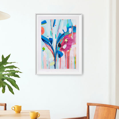 Framed abstract artwork with colorful design on a white wall above a table